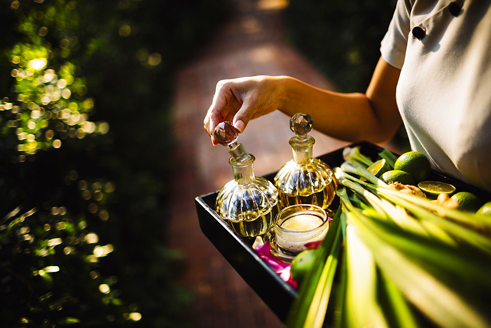 High angle close up of woman holding tray with glass bottles, candles and fruit, Vietnam