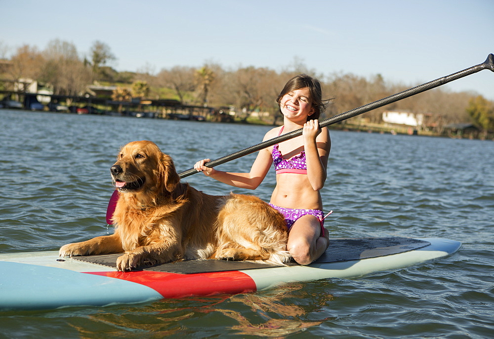 A child and a retriever dog on a paddleboard on the water, Austin, Texas, USA