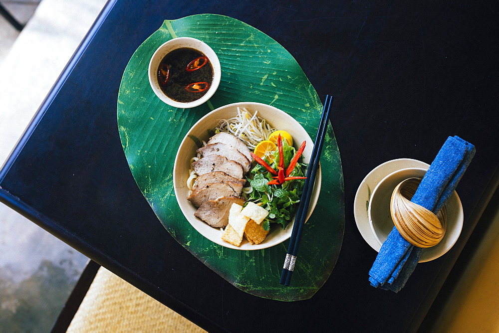 High angle close up of bowl of Cao Lau noodles with grilled pork and herbs, Vietnam