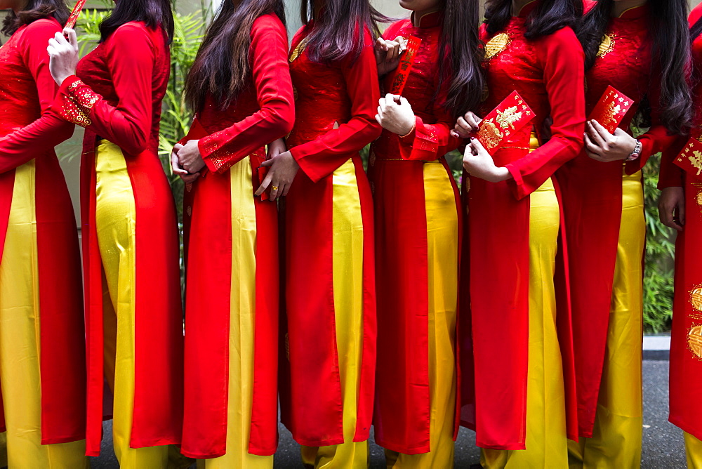 Close up of line of young women in traditional red and yellow dress outside of a wedding, Vietnam