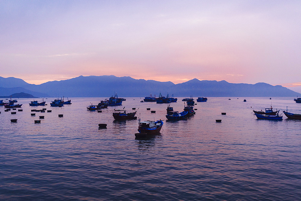 Large group of fisherman in traditional fishing boats on lake at sunrise, mountains in the distance, Vietnam