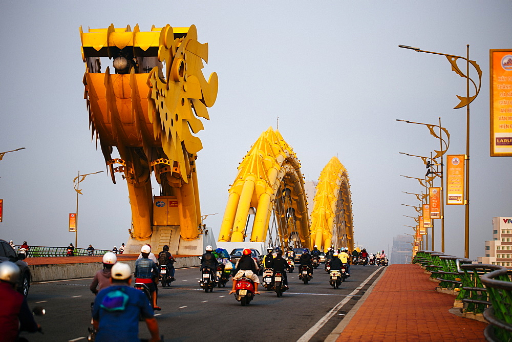 Rear view of commuters on motorcycles crossing bridge in the shape of a dragon, Vietnam