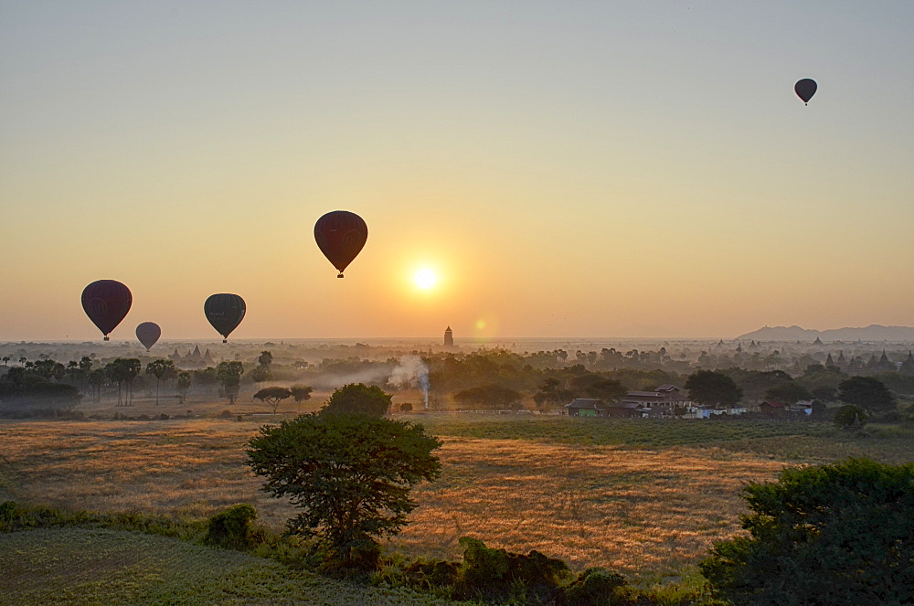 Hot air balloons over landscape with distant temples at sunset, Bagan, Myanmar