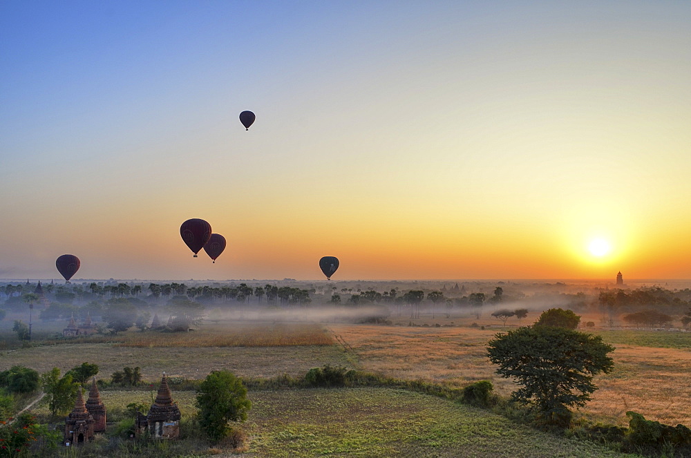 Hot air balloons over landscape with distant temples at sunset, Bagan, Myanmar