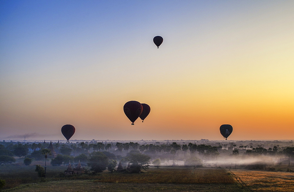 Hot air balloons over landscape with distant temples at sunset, Bagan, Myanmar