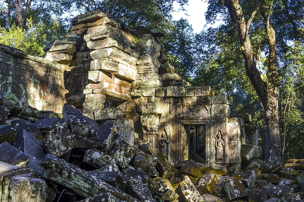 Ankor Wat, a 12th century historic Khmer temple and UNESCO world heritage site. Arches and carved stone blocks in ruins of temple pavilions, with trees dominating the buildings, Angkor Wat, Cambodia