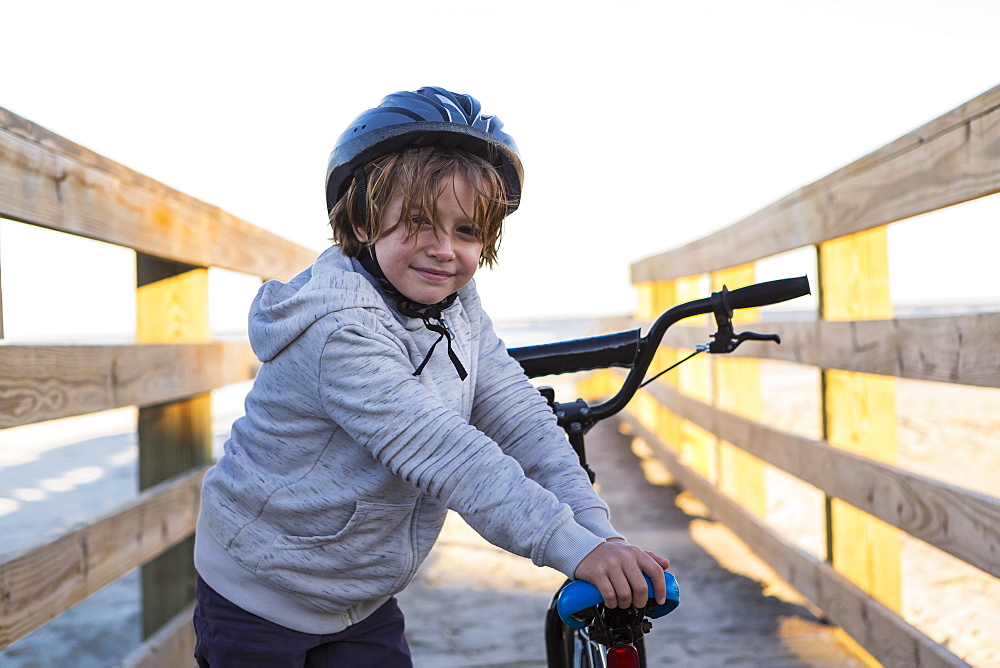 A boy on a bicycle, with helmet on a walkway on the beach, St Simon's Island, Georgia, United States