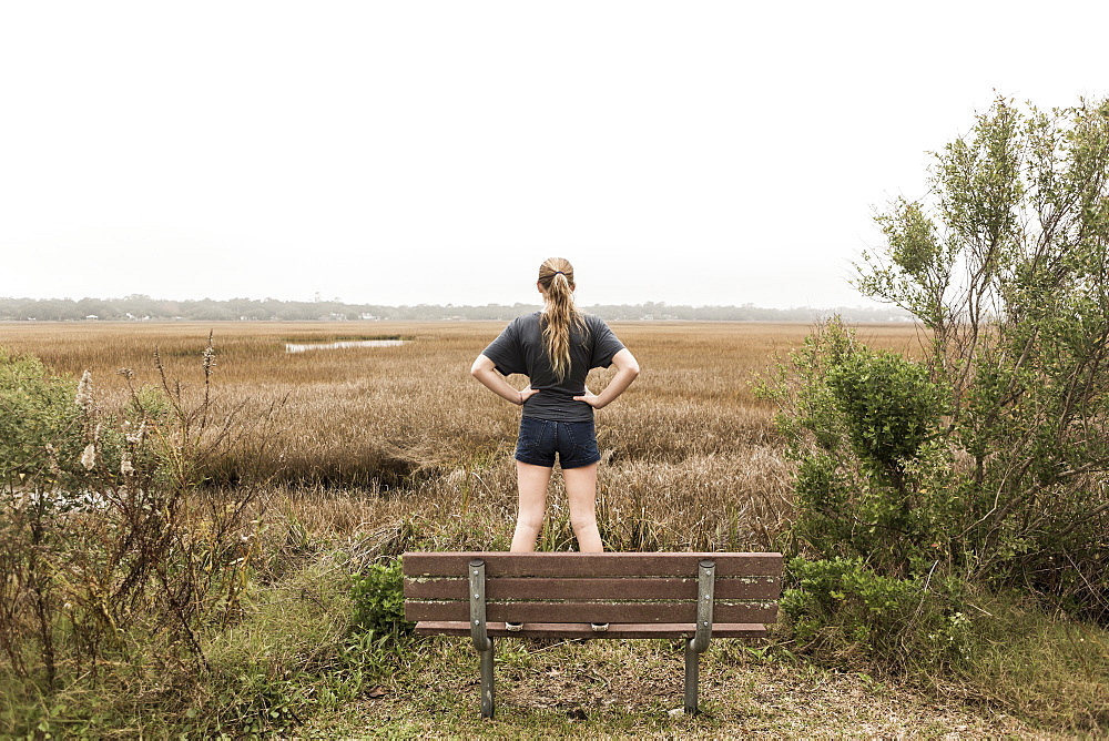 Teenage girl standing on a bench looking out over marshes, St Simon's Island, Georgia, United States