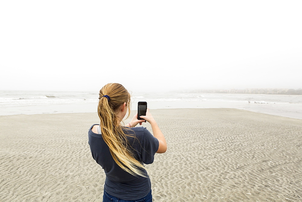 A teenage girl talking pictures with smart phone at the beach, St Simon's Island, Georgia, United States