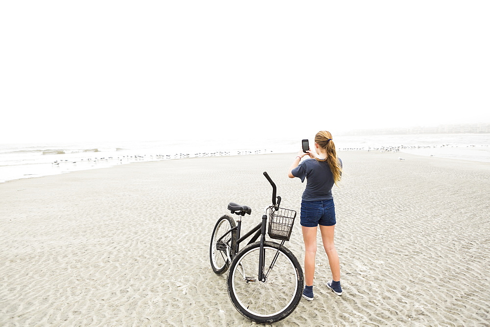 A teenage girl talking pictures with smart phone at the beach, St Simon's Island, Georgia, United States