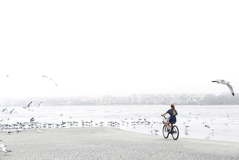A teenage girl biking on a sandy beach by the ocean, St Simon's Island, Georgia, United States
