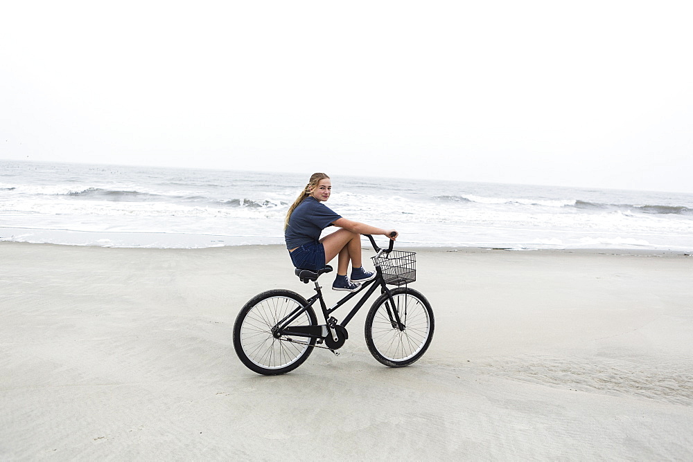 A teenage girl biking on a sandy beach by the ocean, St Simon's Island, Georgia, United States