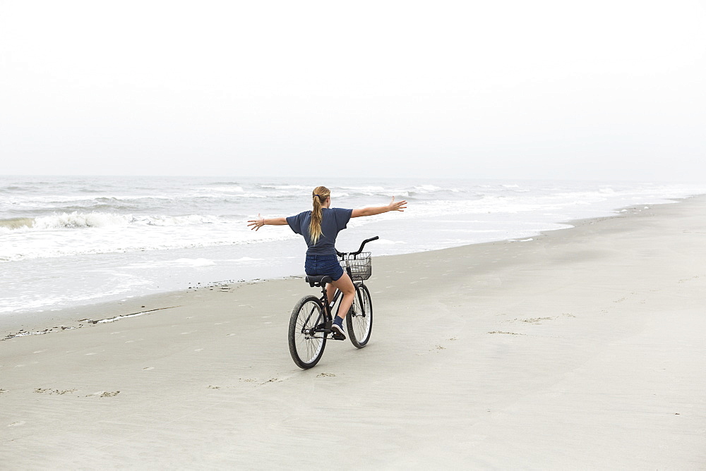 A teenage girl biking on a sandy beach by the ocean, St Simon's Island, Georgia, United States