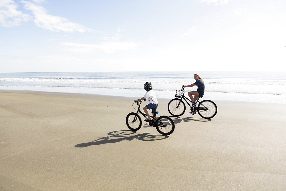 Siblings, a boy and girl cycling on a beach, St Simon's Island, Georgia, United States