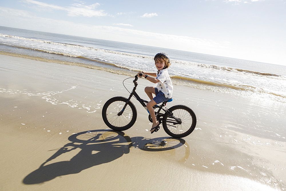 A young boy biking on a sandy beach, St Simon's Island, Georgia, United States
