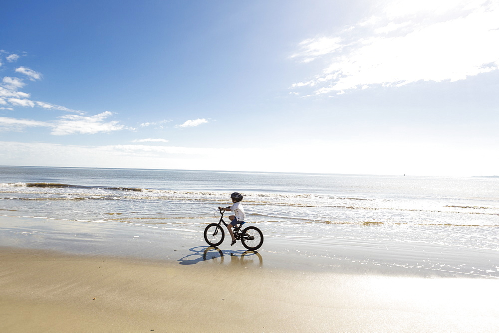 A young boy biking on a sandy beach, St Simon's Island, Georgia, United States