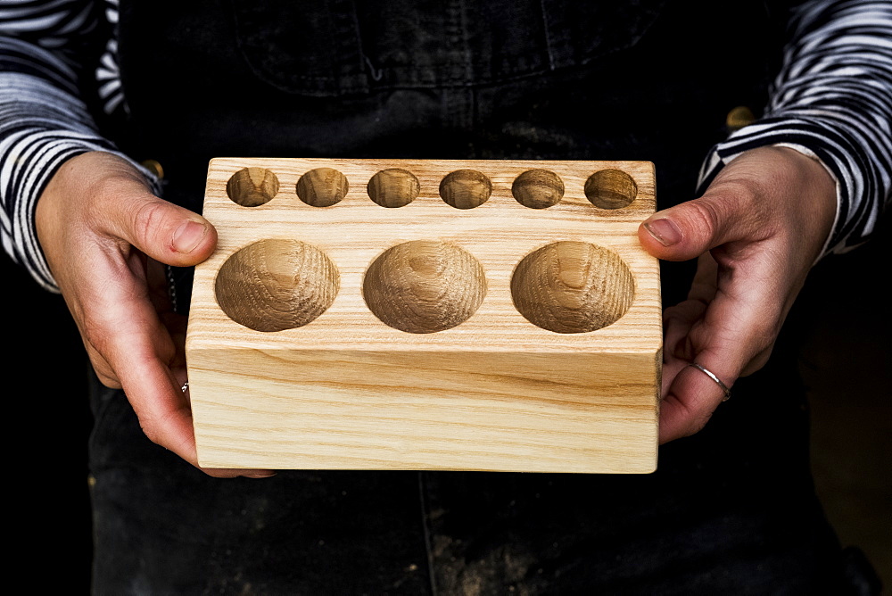 Close up of person holding wooden block with circular holes in different sizes, Oxfordshire, United Kingdom