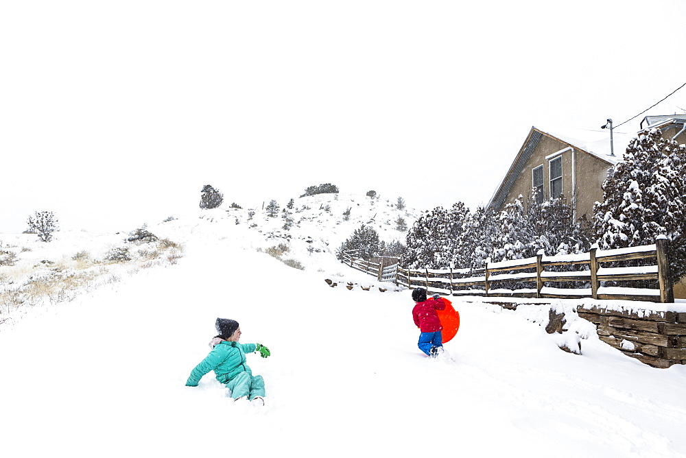 A boy and girl sledding down hill in snow, United States