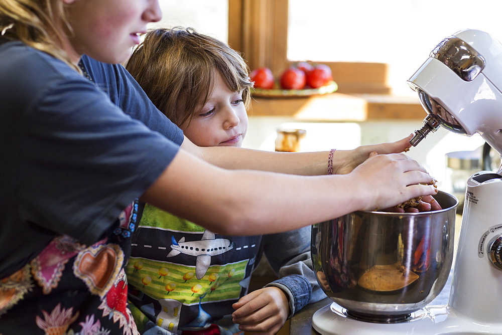 A teenage girl and her 6 year old brother in a kitchen, using a mixing bowl, United States