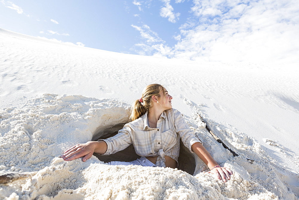 A teenage girl emerging from a dug out hole in white sand dunes, White Sands National Monument, New Mexico, United States