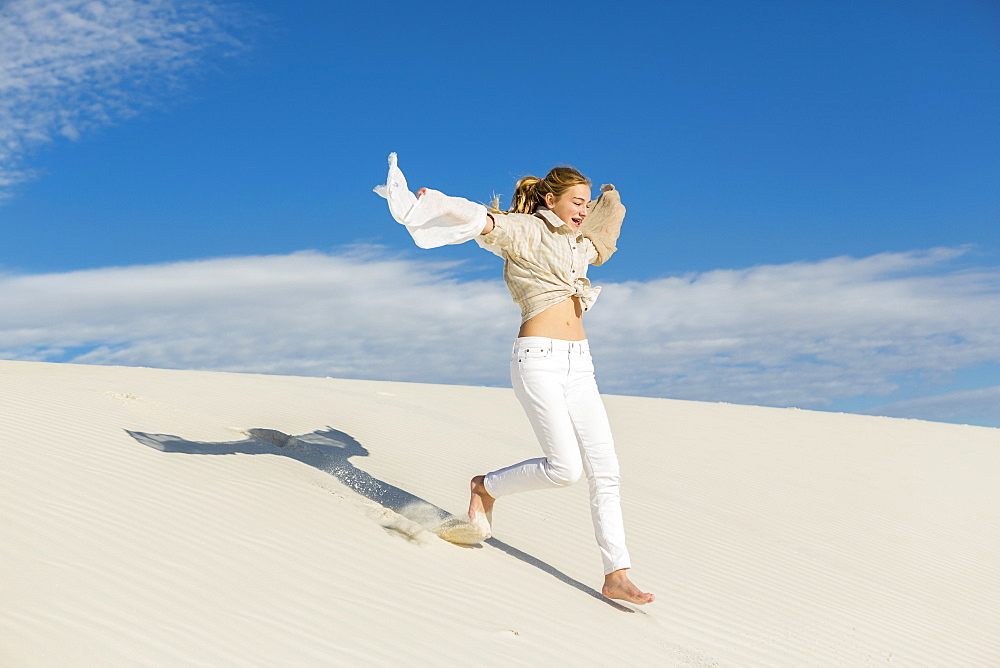 A teenage girl leaping and dancing in light white sand in a dunes landscape, White Sands National Monument, New Mexico, United States