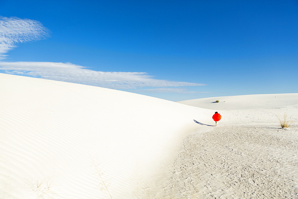 A young boy carrying an orange sled in a white undulating dune landscape, White Sands National Monument, New Mexico, United States