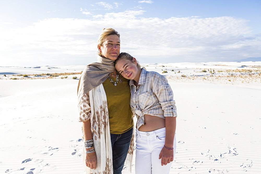 A mother and her teenage daughter side by side, arms around waists, in an open space, White Sands National Monument, New Mexico, United States