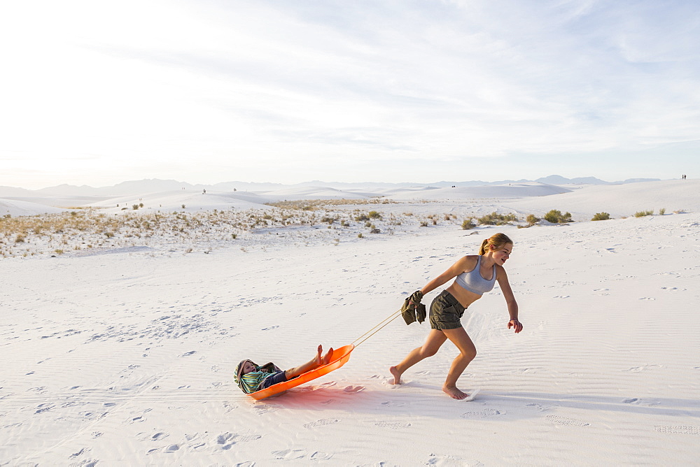 A teenage girl pulling her brother in sled at sunset, White Sands National Monument, New Mexico, United States