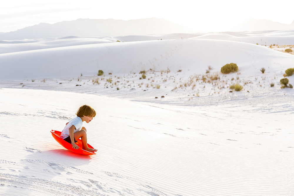 A young boy sledding down white sand dunes, White Sands National Monument, New Mexico, United States