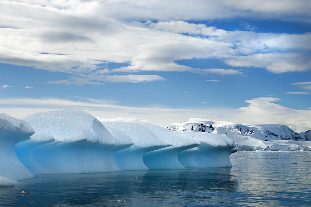 Mountains and snowy landscape reflected in calm sea water. Ice formations shaped into overhangs and smoothed by weathering, Antarctica