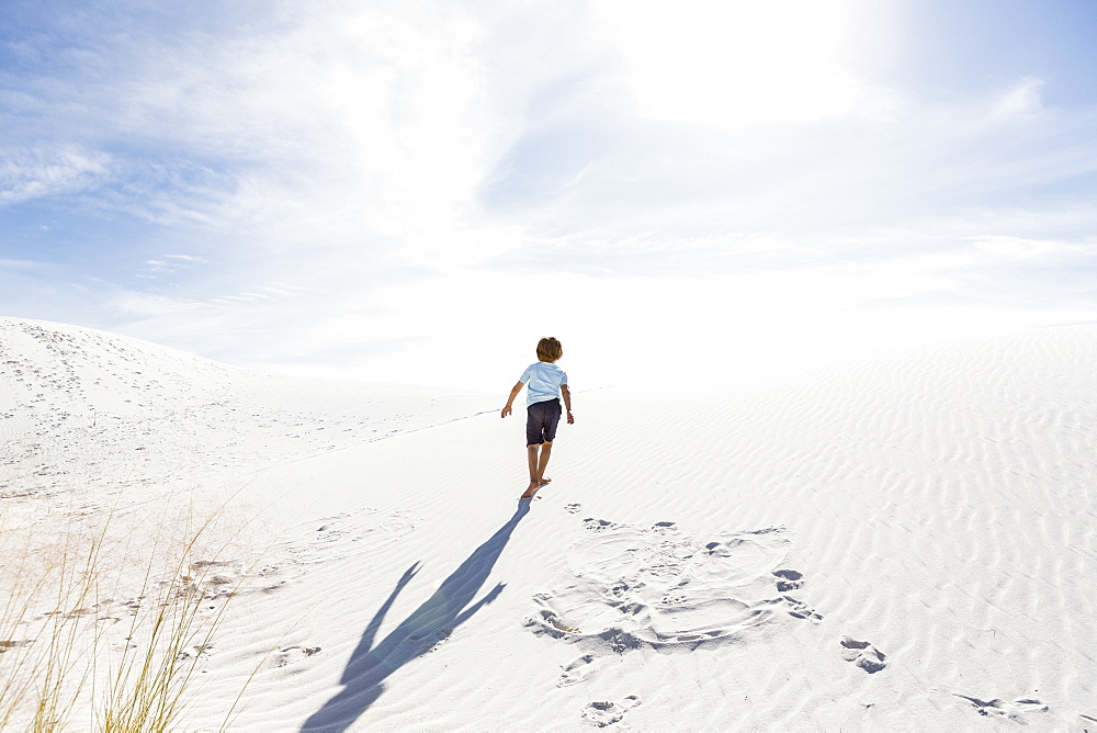 A young boy climbing up white sand dune, White Sands National Monument, New Mexico, United States