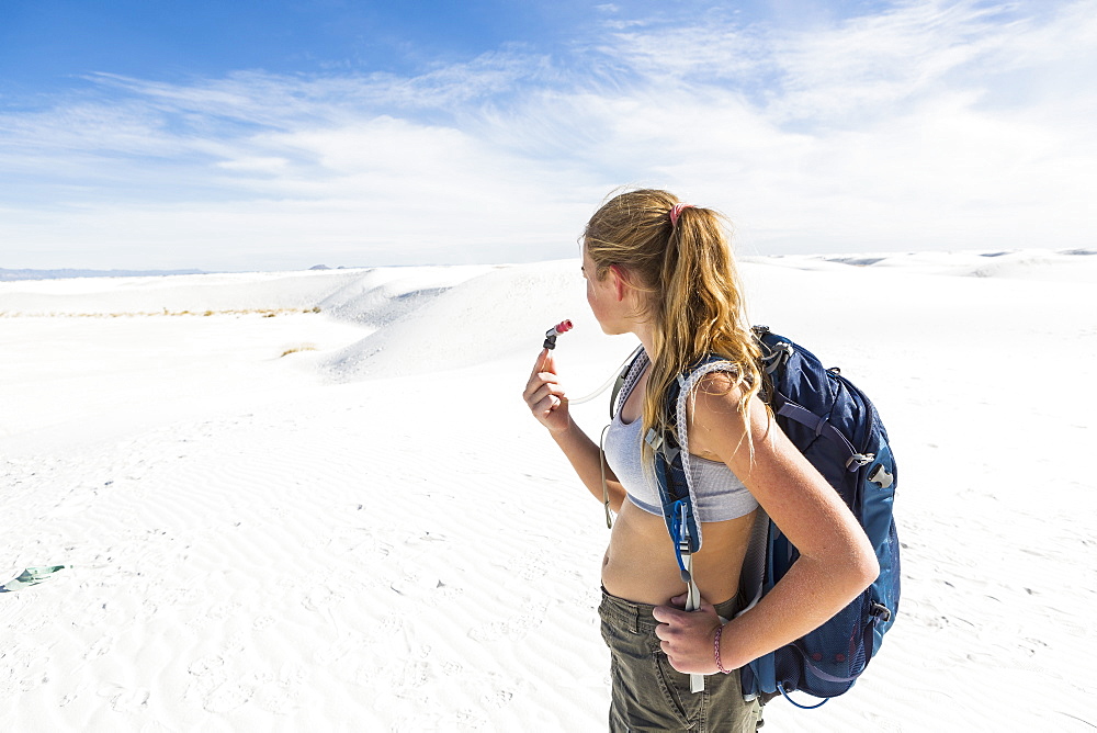 A teenage girl hiking across white sand dunes, White Sands National Monument, New Mexico, United States