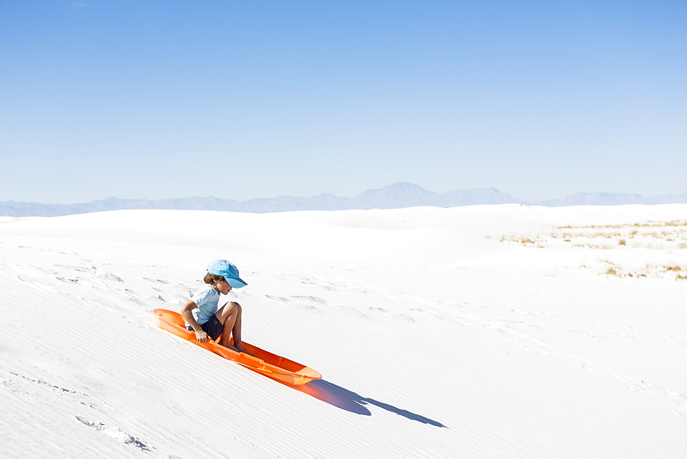 A young boy sledding on sand dune, White Sands National Monument, New Mexico, United States