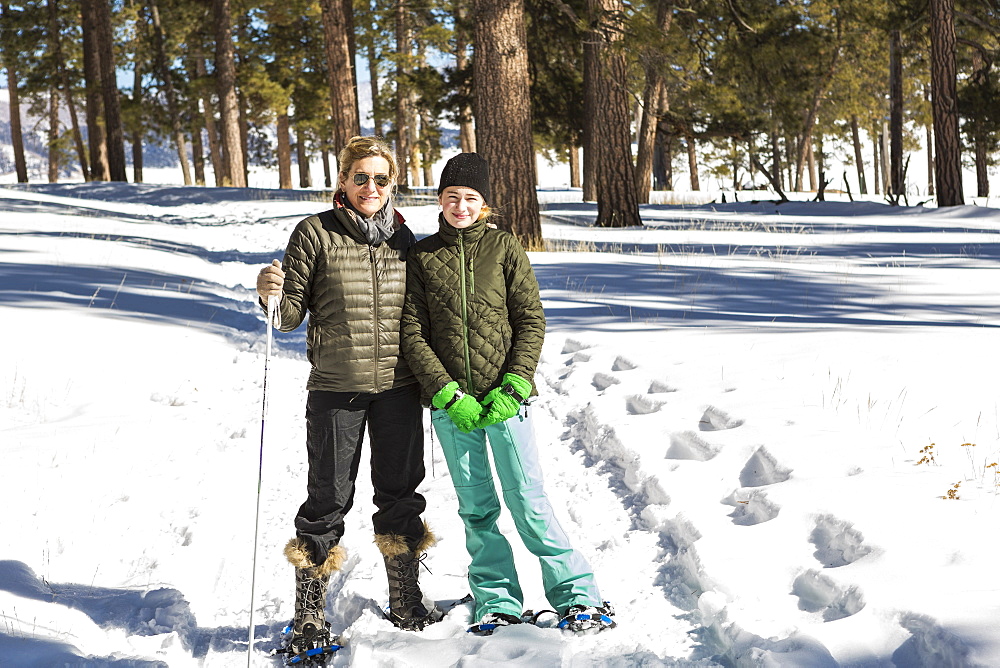 An adult woman and teenage girl in snow shoes in woodland holding ski poles