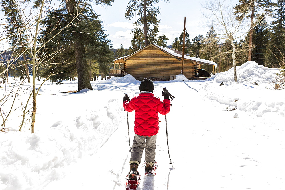 Rear view of young boy in a red jacket snow shoeing