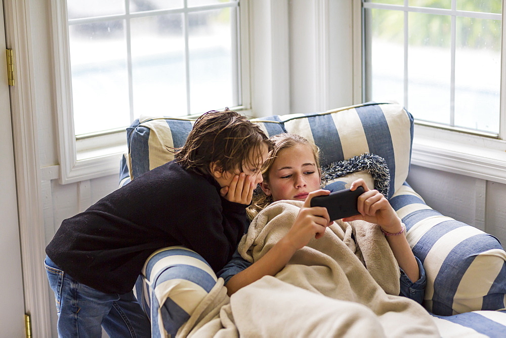 A boy and a teenage girl looking at the screen of a smart phone.