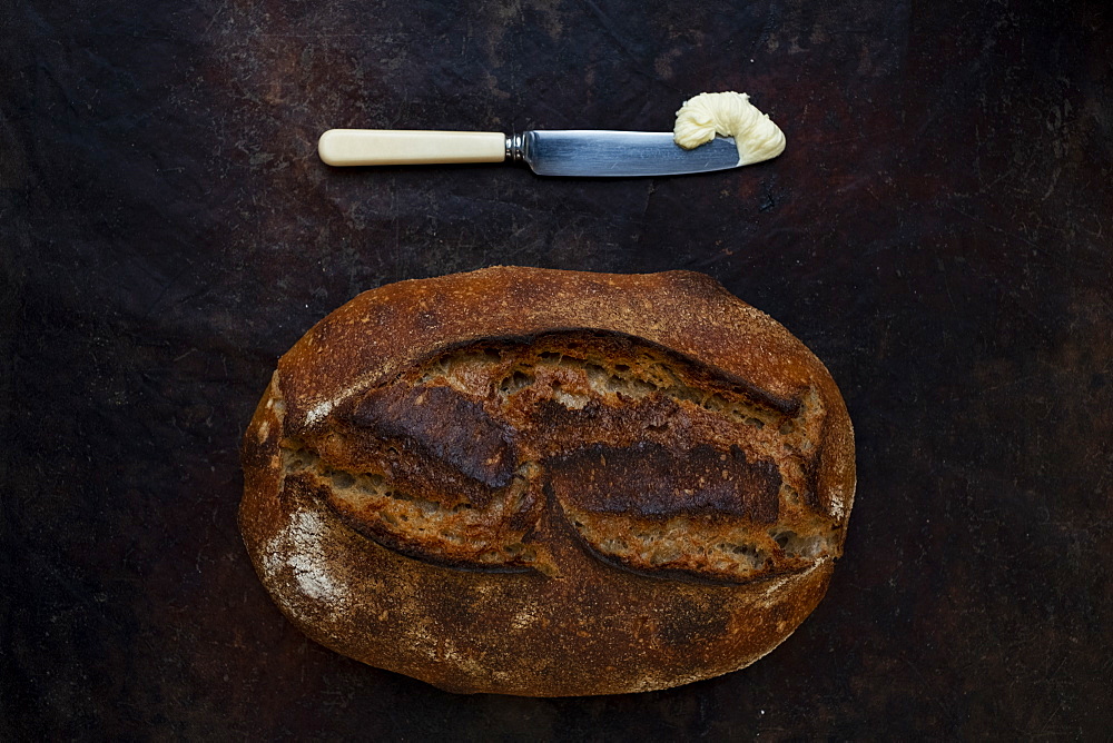 Freshly baked loaf of bread in an artisan bakery with a knife and portion of butter.