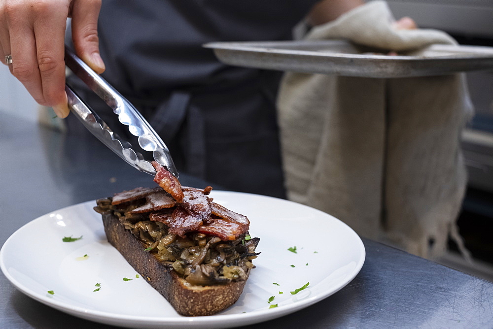 High angle close up of chef preparing toasted bread with bacon and mushrooms in an artisan bakery.