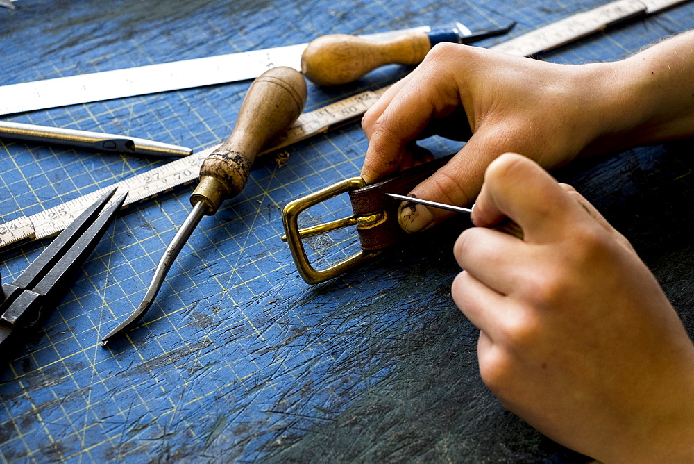 High angle close up of person working in saddler's workshop, attaching buckle to leather strap, Berkshire, United Kingdom