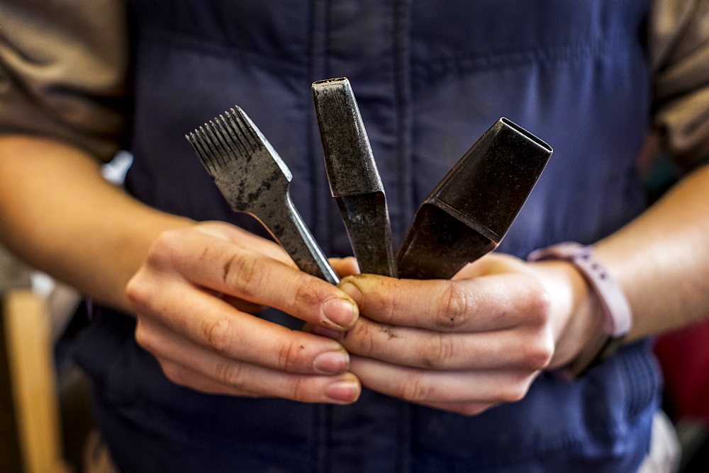 Close up of person holding three metal saddle making tools, Berkshire, United Kingdom