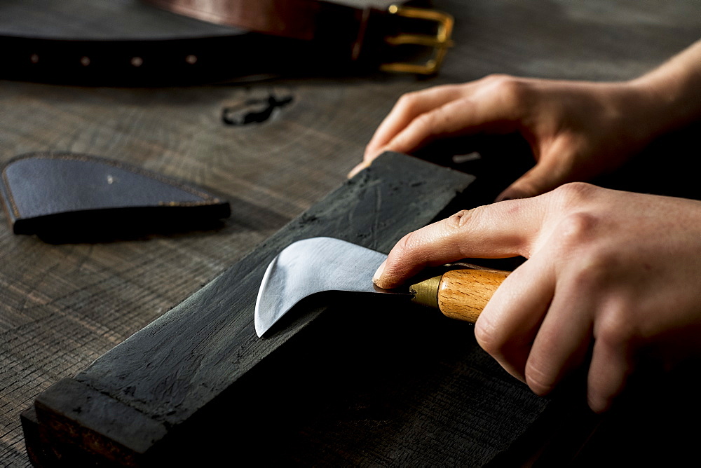 High angle close up of person sharpening saddle making tool on whetstone, Berkshire, United Kingdom