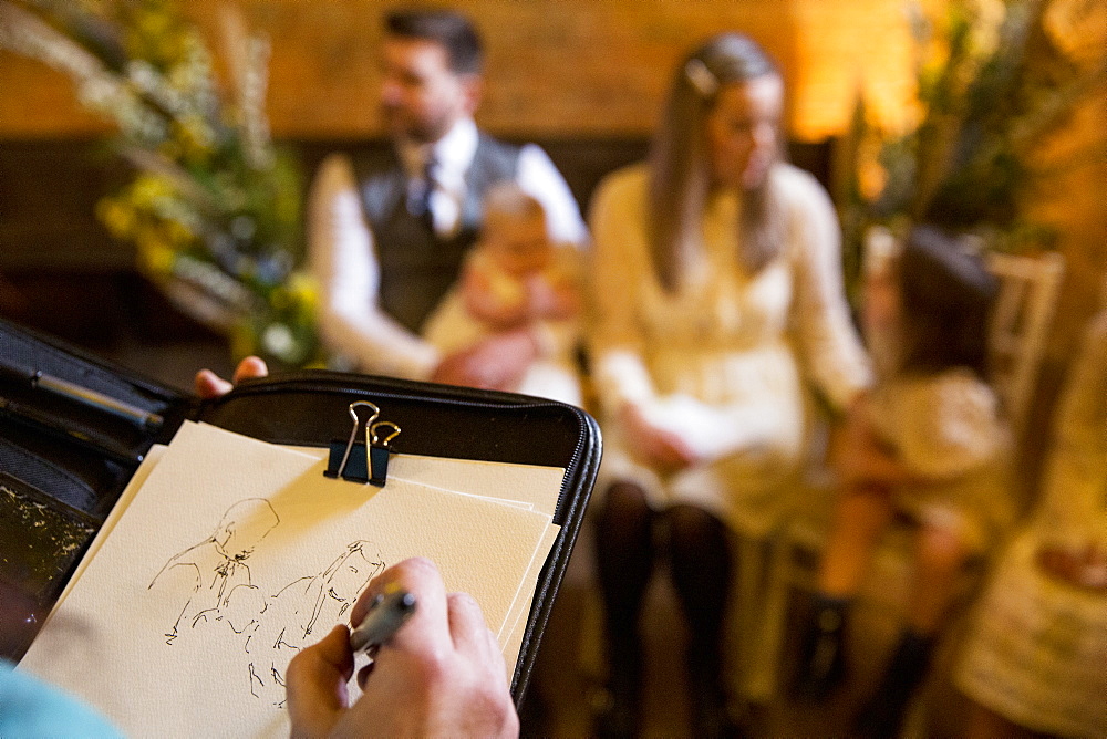 Over the shoulder view of artist sketching family during naming ceremony in an historic barn