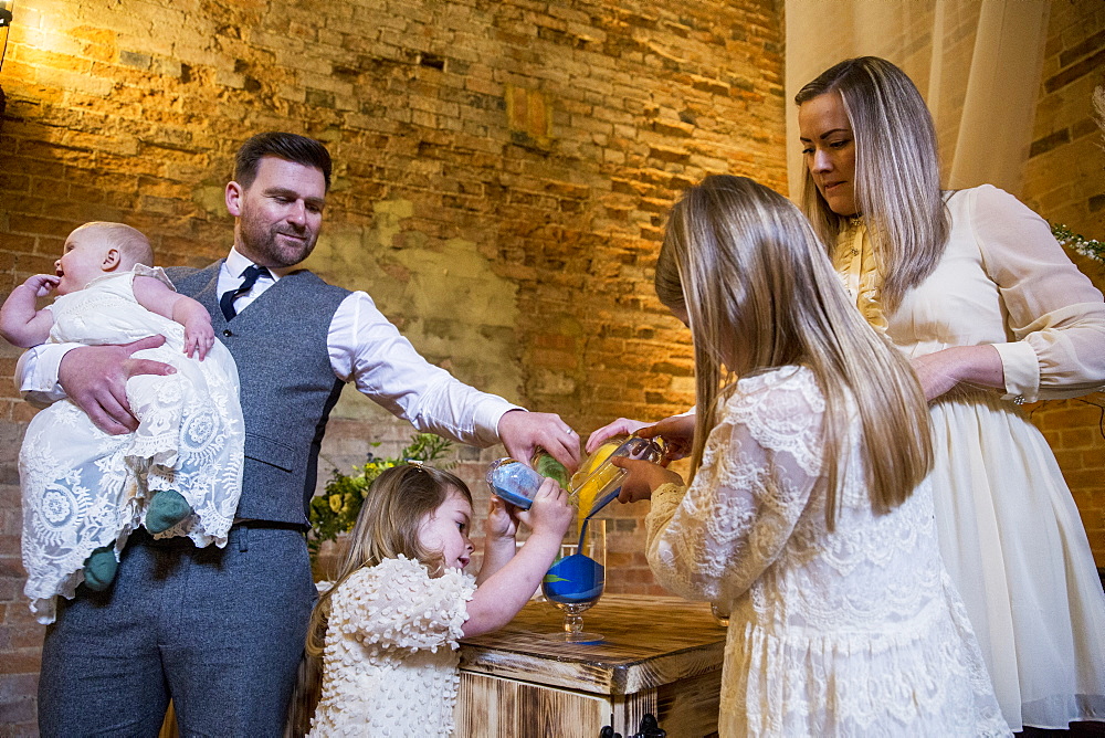 Family pouring coloured sand into glass jar during naming ceremony in an historic barn