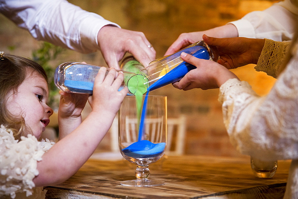 Family pouring coloured sand into glass jar during naming ceremony in an historic barn