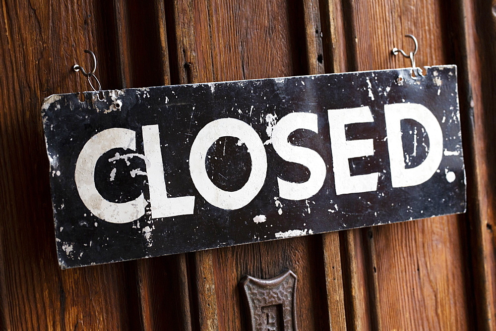 Close up of black and white closed sign on wooden door of a cafe