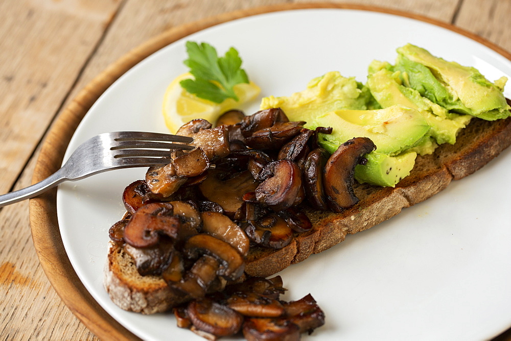 High angle close up of Chestnut mushrooms and avocado on toasted sourdough bread on a plate