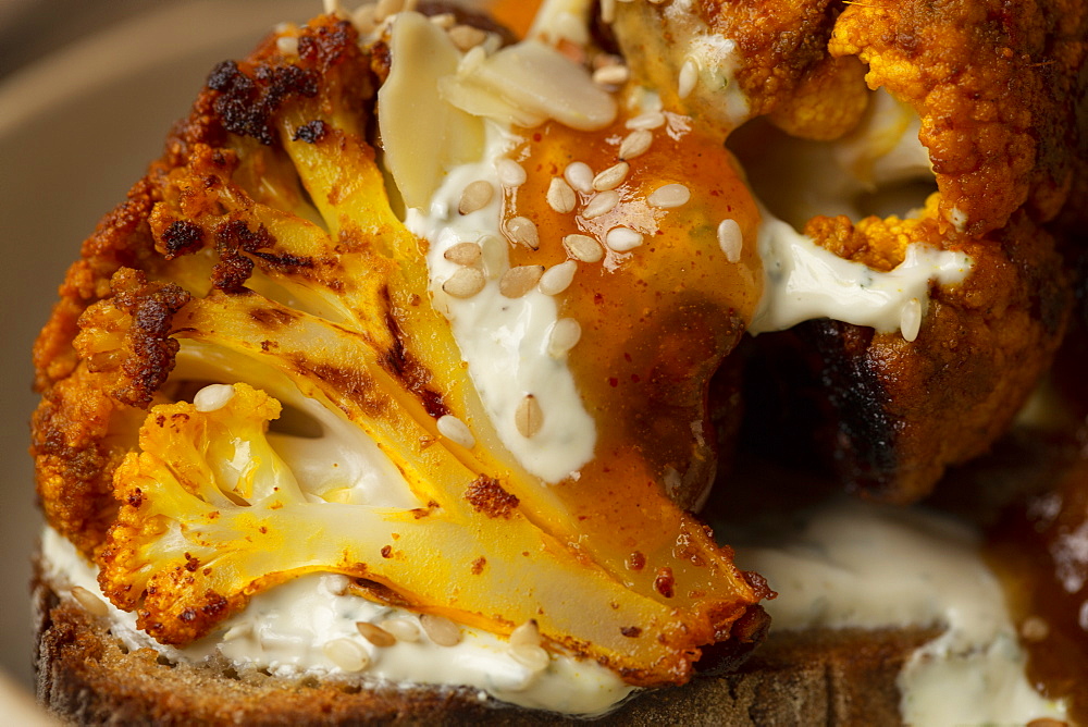 High angle close up of roasted cauliflower with yoghurt and sesame seeds on toasted sourdough bread in a cafe