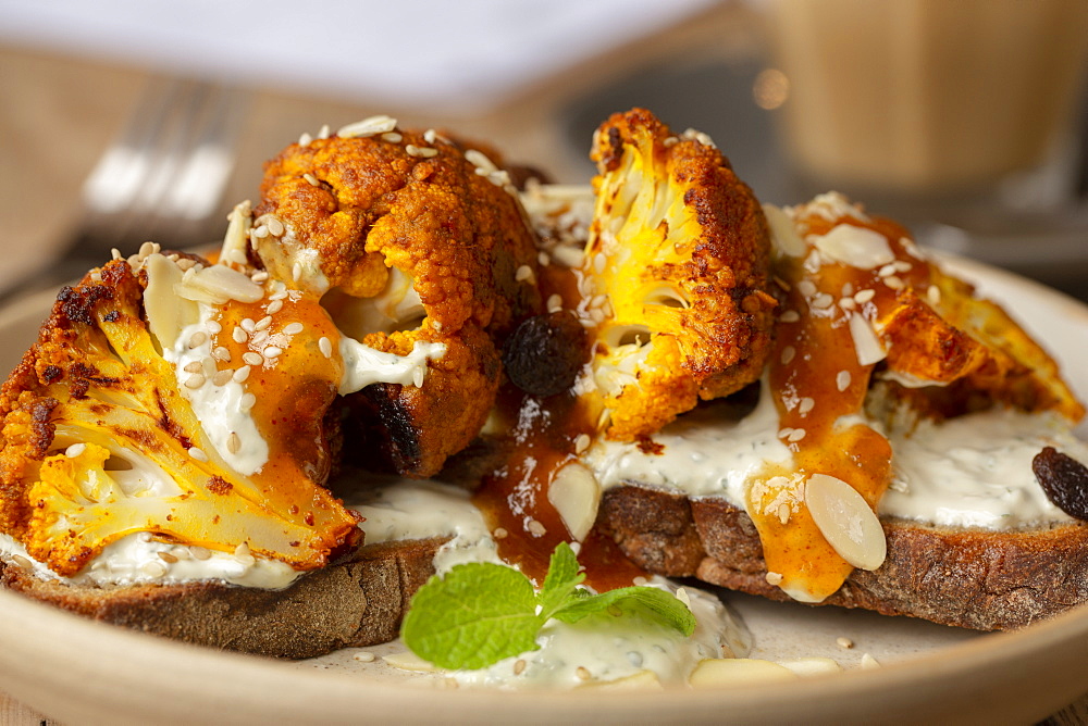 High angle close up of roasted cauliflower with yoghurt and sesame seeds on toasted sourdough bread in a cafe