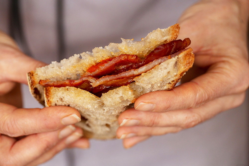 Close up of person holding bacon sandwich with tomato sauce