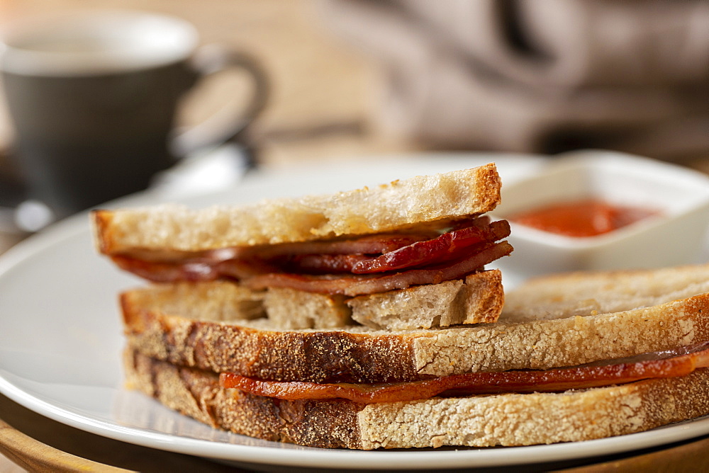 Close up of bacon sandwich and small bowl of home made tomato sauce in a cafe